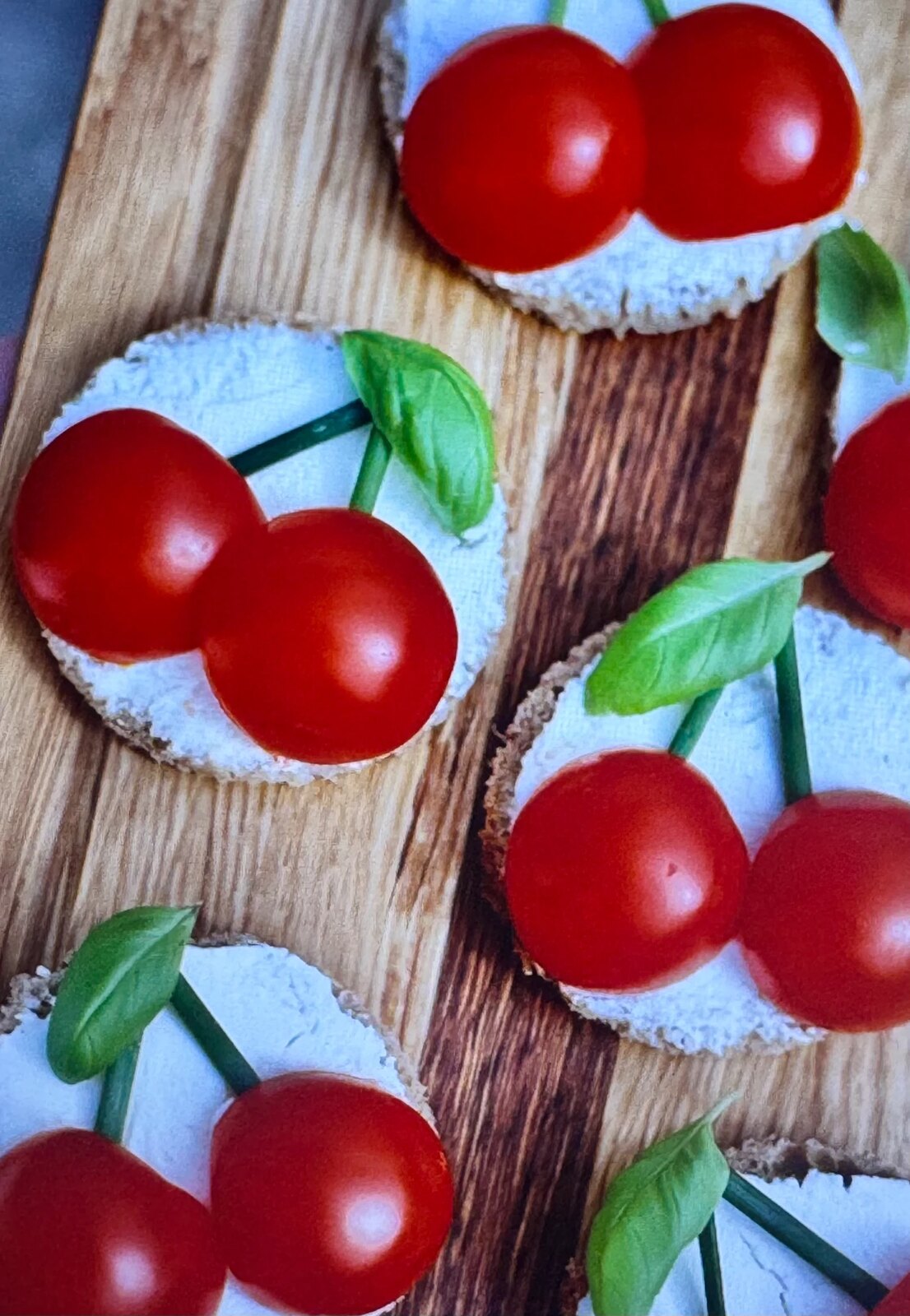Cherry-tomato cherries on cream cheese rounds with basil leaves